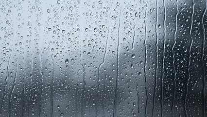 Close-up view of raindrops on a windowpane, with streaks of water flowing down.