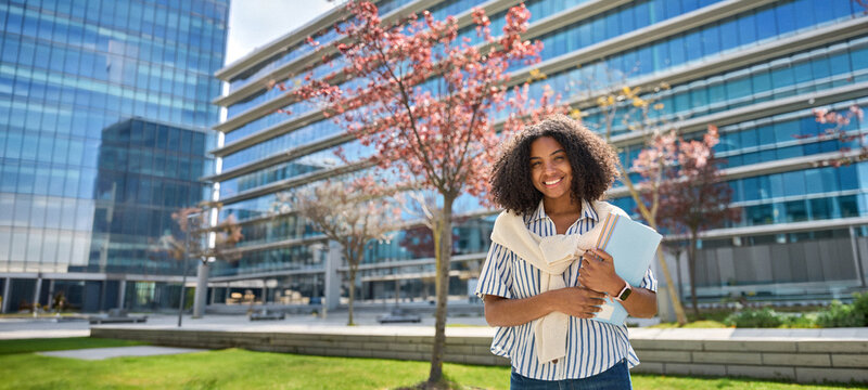 Happy smiling African American girl student standing outside university looking at camera outdoors, portrait. Applying foreign university, study abroad, admission and scholarship program. Banner