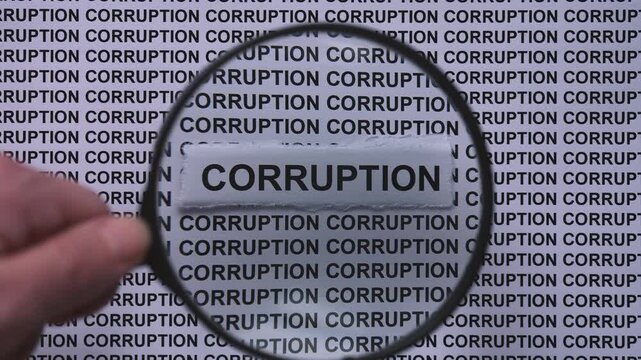 A person with a magnifying glass in his hand magnifying the words Corruption on a newspaper print background. Close up.