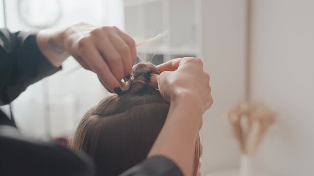 Closeup hair styling in bright salon, stylist sections blonde tresses with gentle hands, secures sections with clip to form sleek bun, soft natural light, calm modern interior, detailed stepbystep