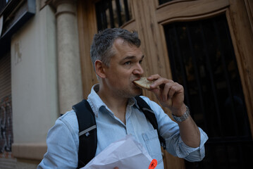 Customer in denim shirt eating a slice of bread outdoors next to wooden doorway