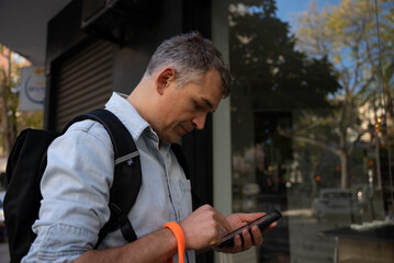 Middle-aged man with backpack using smartphone outdoors in urban environment