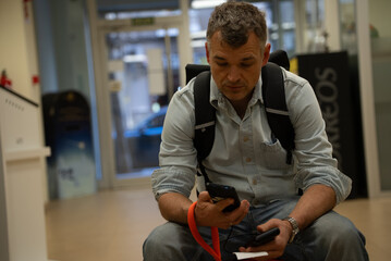 Middle-aged man holding two phones and receipt while seated in postal office lobby