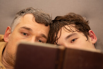 Father and son lying close reading a book with only their eyes visible focused on the pages