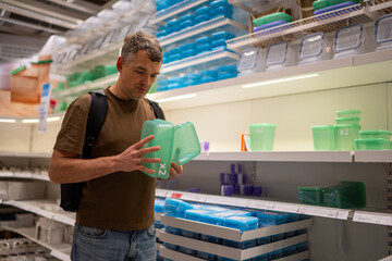 Man with backpack inspecting plastic containers on a shelf in a store aisle