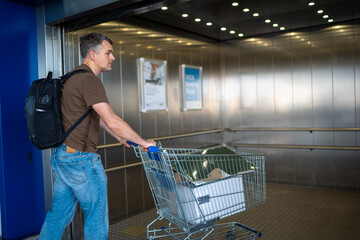 Man with a backpack pushing a shopping cart inside a metallic elevator in a retail environment
