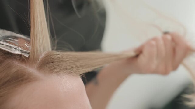 closeup caucasian woman hair sectioning foiling professional colorist applies bleach and toner with foil stylist combs roots precise parting smoothing neutral studio background calm focused atmosphere