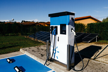 Electric vehicle charging station with multiple connectors, surrounded by solar panels and green grass, showcasing sustainable energy solutions in modern transportation