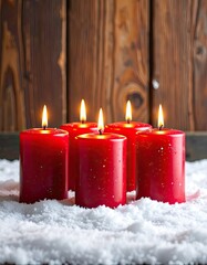 Five lit red pillar candles glowing warmly against a rustic wooden background surrounded by snow.