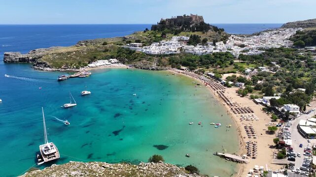 Aerial drone cinematic video of paradise organized main beach of Lindos with amazing turquoise waters, Rhodes island, Dodecanese, Greece