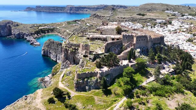 Aerial drone cinematic video of archaeological site of Acropolis of Lindos vilage featuring amazing organized beach and iconic Saint Paul bay, Rhodes island, Dodecanese, Greece