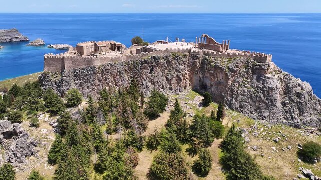 Aerial drone cinematic video of archaeological site of Acropolis of Lindos vilage featuring amazing organized beach and iconic Saint Paul bay, Rhodes island, Dodecanese, Greece