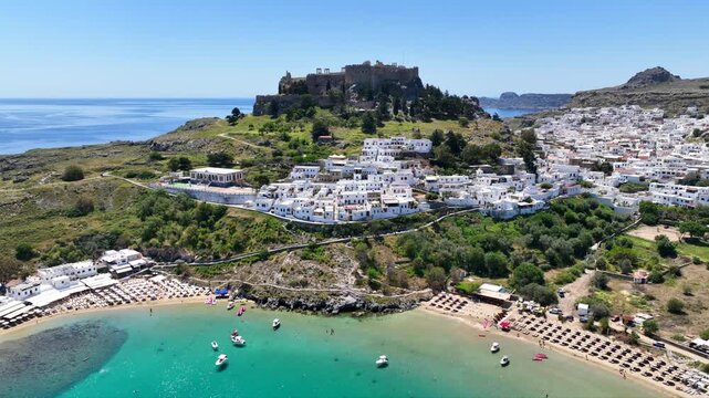 Aerial drone cinematic video of archaeological site of Acropolis of Lindos vilage featuring amazing organized beach and iconic Saint Paul bay, Rhodes island, Dodecanese, Greece