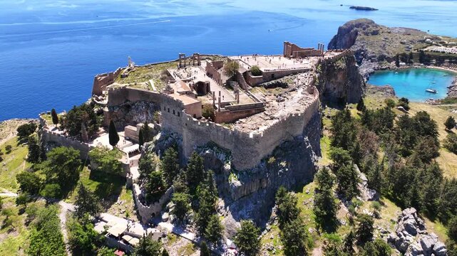 Aerial drone video of iconic archaeological site of Acropolis of Lindos built uphill featuring picturesque village, amazing organized beach and Saint Paul bay, Rhodes island, Dodecanese, Greece