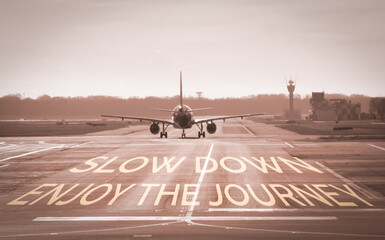 Plane taxiing down runway with Slow down enjoy the journey painted on the tarmac, promoting mindful travel, stress free trips, relaxation and appreciating the journey ahead