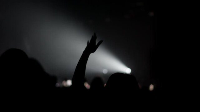 Backlit crowd with raised hand reaching toward bright stage light during live music event creating emotional concert atmosphere and sense of unity