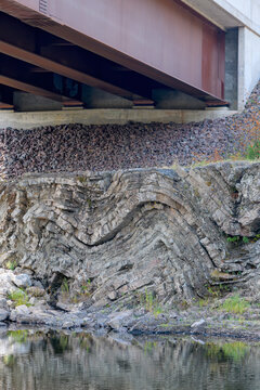 A geologic fold in sedimentary rock under a bridge over a brook. Many layers of rock.