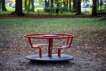 An empty red carousel in a city park. Fallen yellow leaves surround the carousel.