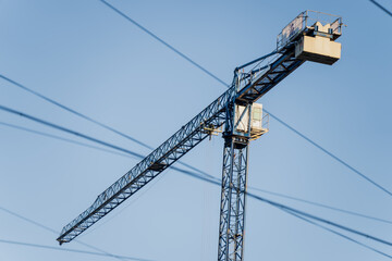 Tower crane structure against clear sky with intersecting overhead lines, illustrating heavy construction equipment, building industry operations, and urban development projects