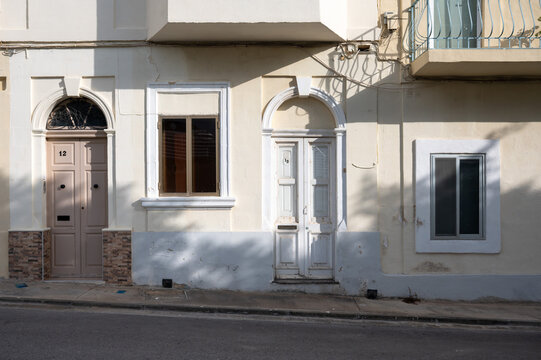 Authentic facades of modest row houses in ochre limestone with colorful doors and windows, showing weathered surfaces and architectural details Cospicua/Bormla, Malta, 10 DEC 2025.