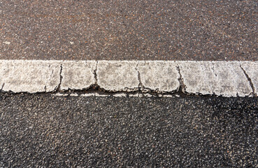 Top-down view of a weathered white painted line on a rough asphalt road surface.