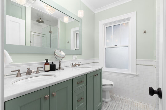 An elegant bathroom featuring a green double vanity and walls with a marble countertop, basketweave marble tile flooring, and glass pendant lights.