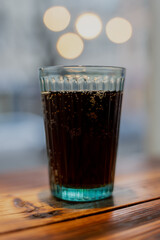 Carbonated soft drink in clear glass on wooden table with bokeh lights, representing modern beverage service and casual dining industry