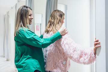 Two women shopping in store trying on clothes in fitting room. High quality photo