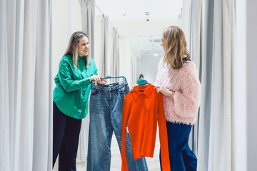 Two women shopping in store trying on clothes in fitting room. High quality photo