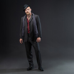 A man dressed in a noir style suit with elements of nonchalance and ethnic style, a charismatic man in a suit and hat in a photo studio on a gray background