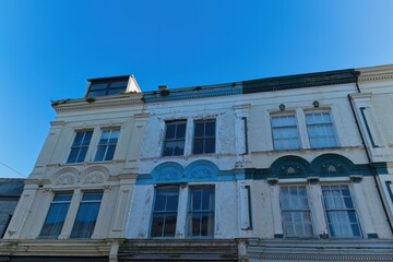 Three adjacent, aged, two-story buildings with ornate facades, painted in faded white, blue, and green, under a clear blue sky, viewed from below in Caernarfon - Gwynedd - Wales - UK
