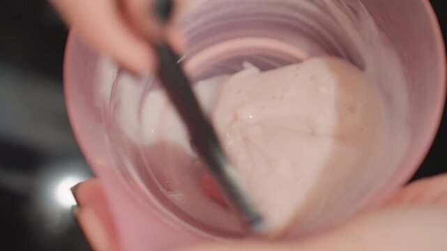 pink cream poured into cup closeup, beautician mixing facial mask using spatula, slow motion swirl revealing glossy silky texture, handheld macro shot capturing product detail, asmr satisfying