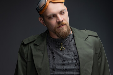 Bald man in dystopian raincoat with textured holes and goggles, charismatic cyberpunk.