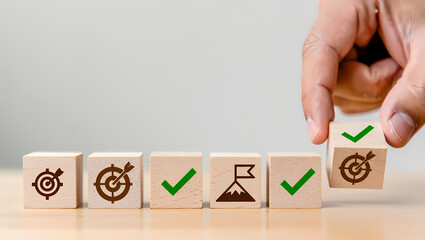 Hand arranging wooden blocks with goal achievement icons, symbolizing business strategy, objectives, and successful project completion