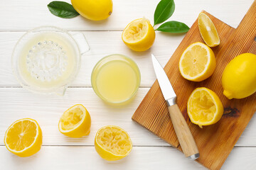 Lemon juice in glass, juicer, knife and fresh lemons on white wooden table, flat lay