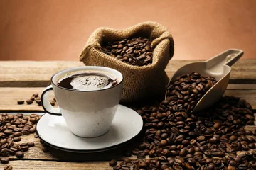 Fototapete Cafe Aromatic coffee in cup and beans on wooden table against brown background, closeup  © New Africa