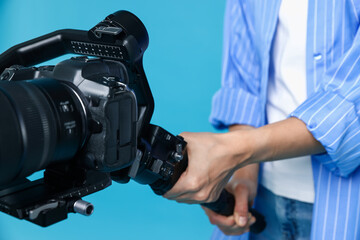 Videographer using gimbal stabilizer with camera on light blue background, closeup © New Africa