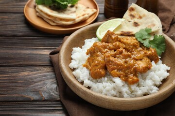 Delicious chicken tikka masala with rice, cilantro, lime and lavash in bowl on wooden table, closeup