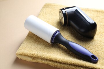 Lint roller, fabric shaver and towel on beige background, closeup