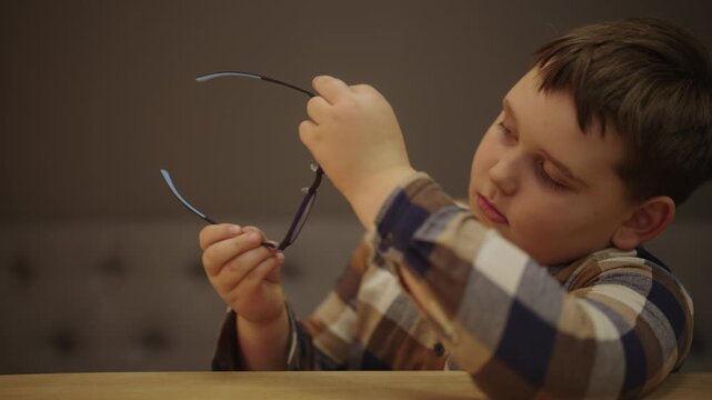 Adorable little boy examining new eyeglasses before putting them on, smiling with satisfaction after correcting vision and being able to see clearly for first time, close-u- portrait, slow motion.