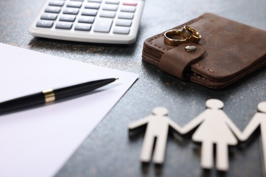 Alimony. Figures of family, pen, document, wedding rings, wallet and calculator on dark table, closeup