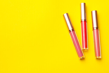 Different lip glosses on yellow background, flat lay. Space for text