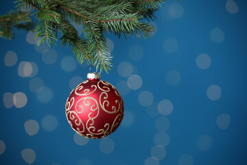 Beautiful ball on Christmas tree branch against blue background, closeup with space for text. Bokeh effect