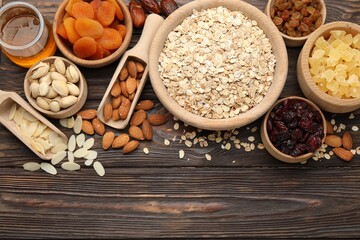 Fototapeta premium Making granola. Oat flakes, dried fruits and other ingredients on wooden table, flat lay. Space for text