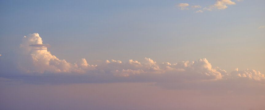 Soft pastel sky with fluffy cumulus clouds illuminated by warm evening light, calm atmospheric landscape, minimal background, peaceful mood, natural weather scene