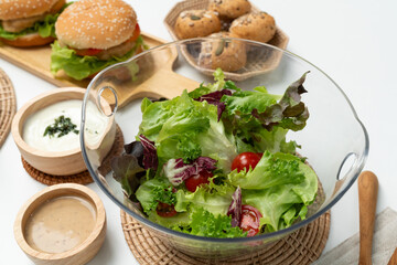 Fresh mix vegetable salad in glass blow beside dish of double meat hamburger and wholegrain bun on meal cooked by homemade serving white table. Preparing special dish menu list's restaurant. Infobahn.