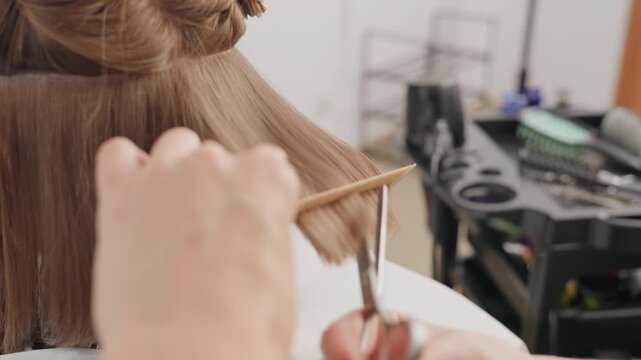 salon stylist trimming blunt bob haircut closeup hands combing sectioned light brown hair, precision shears cutting straight edge, calm studio atmosphere, client seated in cape, trainee observing