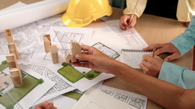 Architect and engineer consider or discuss about building construction using blueprint on table with architectural document, measurement tool and wooden block scatter around at office. Delineation.