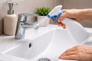 Cleaning bathroom sink with spray bottle and water droplets, hygiene maintenance in modern bathroom with faucet and soap dispenser, fresh and clean environment
