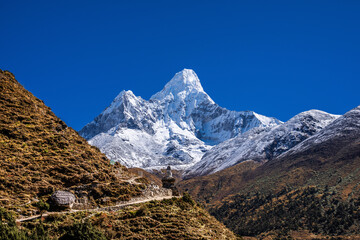 Snowy Mt. Ama Dablam behind the Everest base camp trekking route with a small white stupa and mani stone with engraved mantra "om mani padme hum". Khumbu, Nepal.